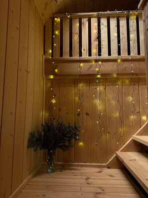 A wooden interior with a balcony, string lights, and a small plant.