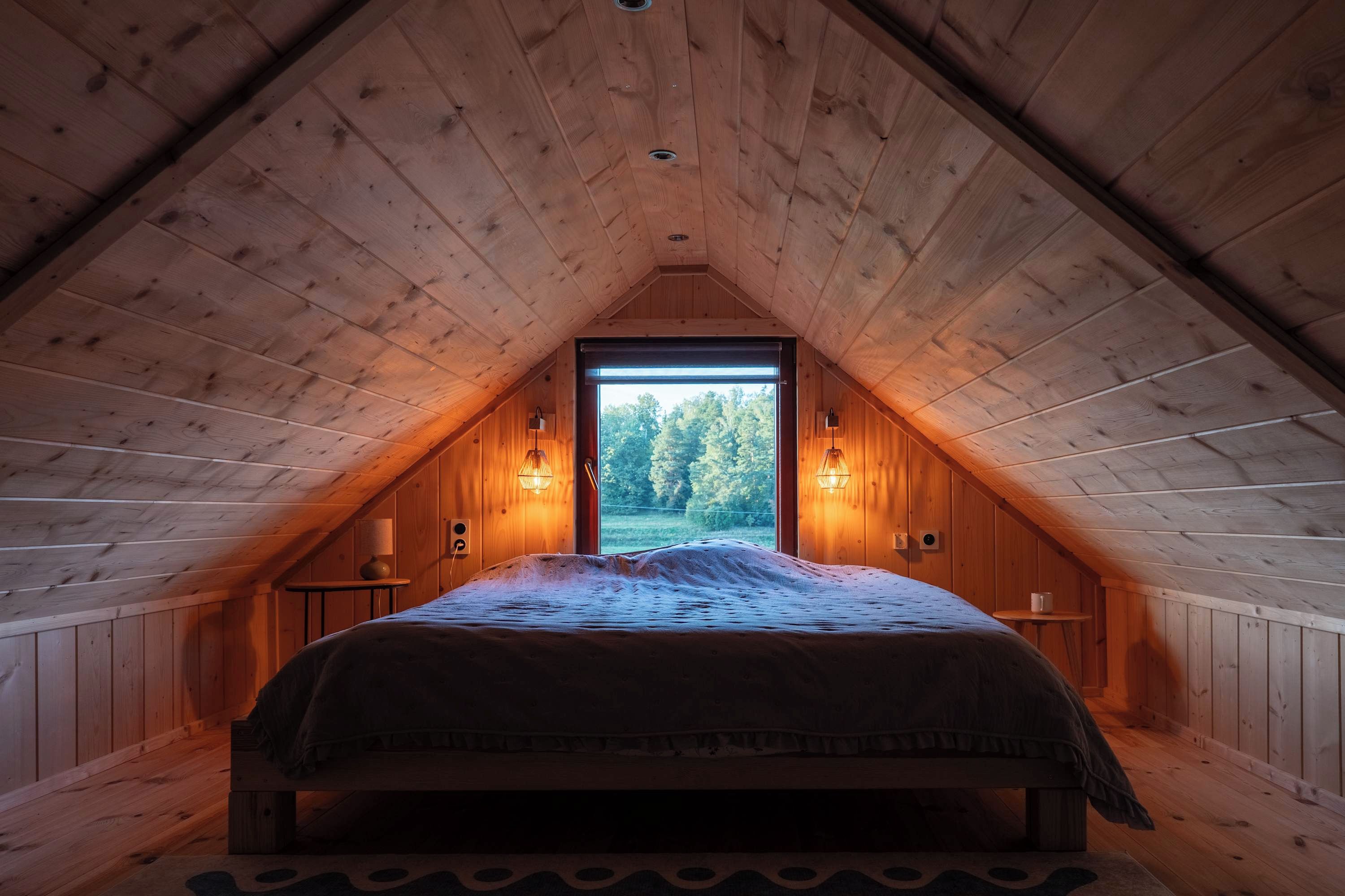 Une chambre confortable située dans les combles, avec un plafond en pente, une grande fenêtre et un lit recouvert d’une couvre-lit à motifs.