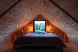 A cozy attic bedroom with a sloped ceiling, a large window, and a bed with a patterned bedspread.