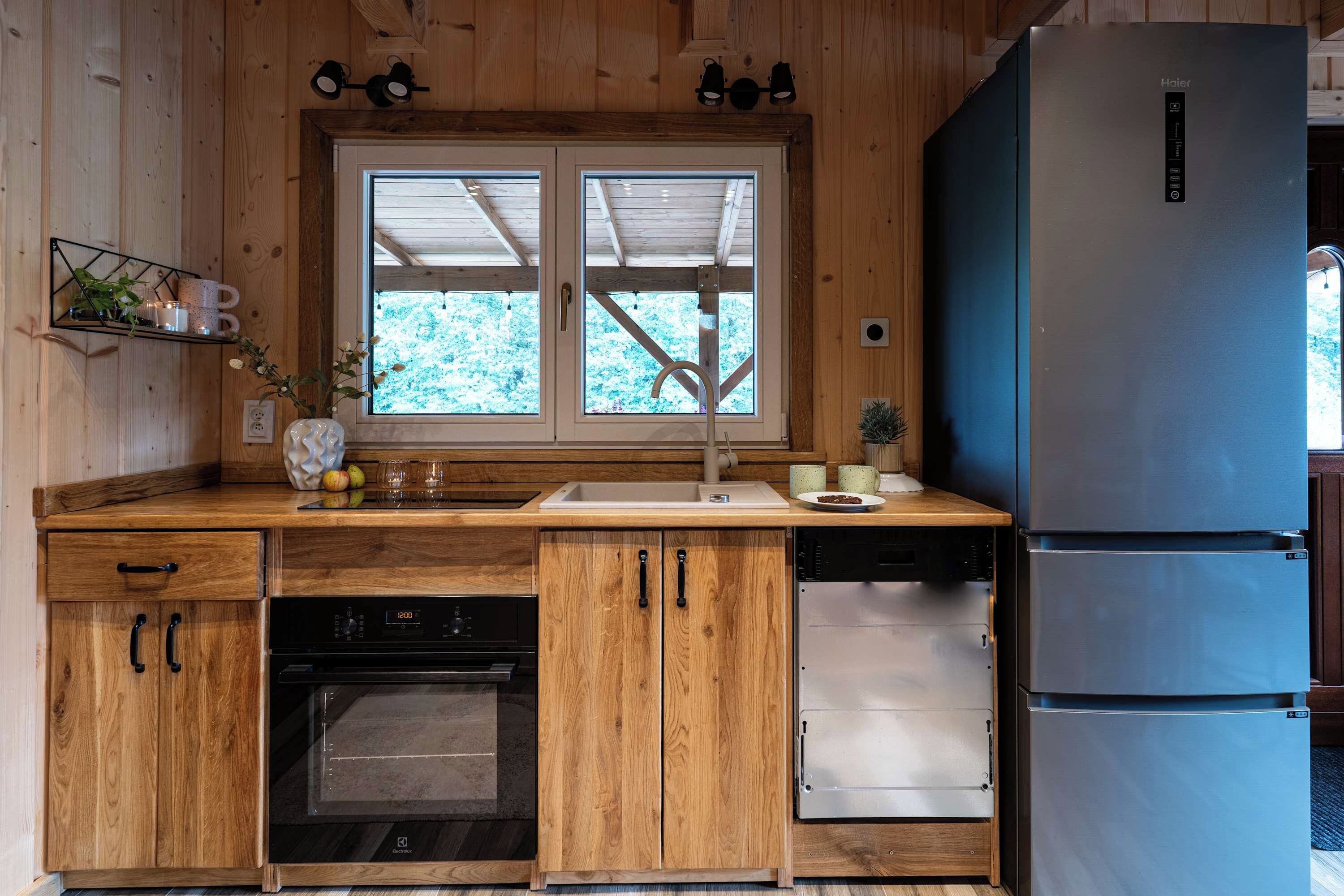 A compact kitchen with wooden cabinetry, a built-in oven, a dishwasher, and a double-door refrigerator.