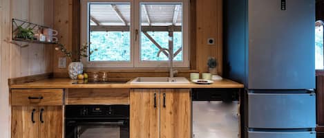 A compact kitchen with wooden cabinetry, a built-in oven, a dishwasher, and a double-door refrigerator.