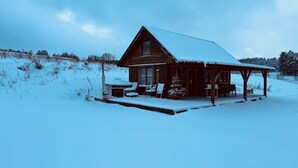 En stuga av trä med ett snötäckt tak och en veranda med sittplatser.