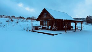 Uma cabana de madeira com telhado coberto de neve e varanda com assentos.