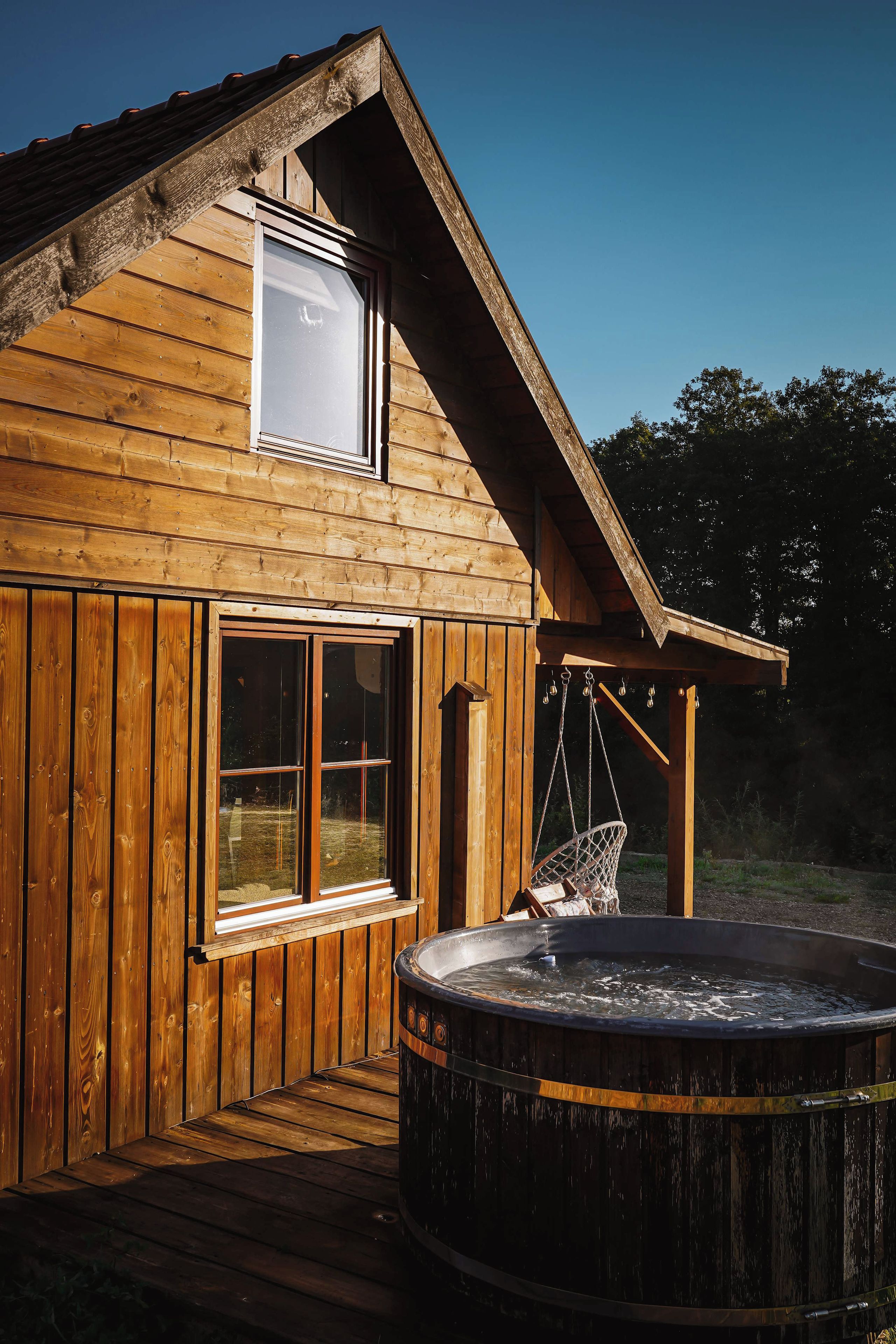 Une cabane en bois avec un jacuzzi, une fenêtre et un fauteuil suspendu.