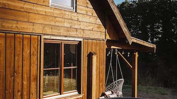 A wooden cabin with a hot tub, a window, and a hanging chair.