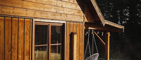A wooden cabin with a hot tub, a window, and a hanging chair.