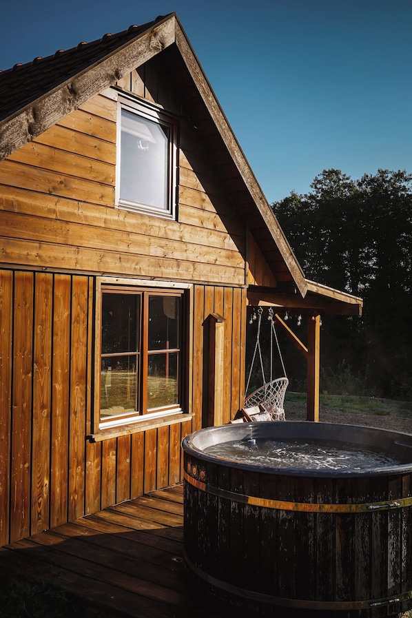 A wooden cabin with a hot tub, a window, and a hanging chair.