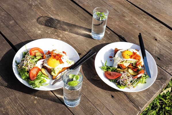 Two plates of food on a wooden table with a glass of water and a knife.