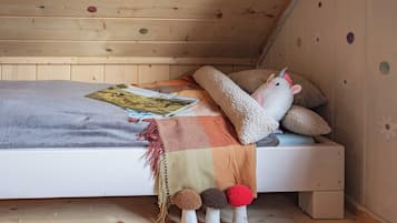 A cozy bedroom with a wooden ceiling, a bed with a blanket, pillows, a stuffed unicorn toy, and a book.