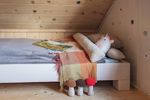 A cozy bedroom with a wooden ceiling, a bed with a blanket, pillows, a stuffed unicorn toy, and a book.