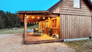 A wooden cabin with a covered porch, outdoor seating, and a view of a forested area.
