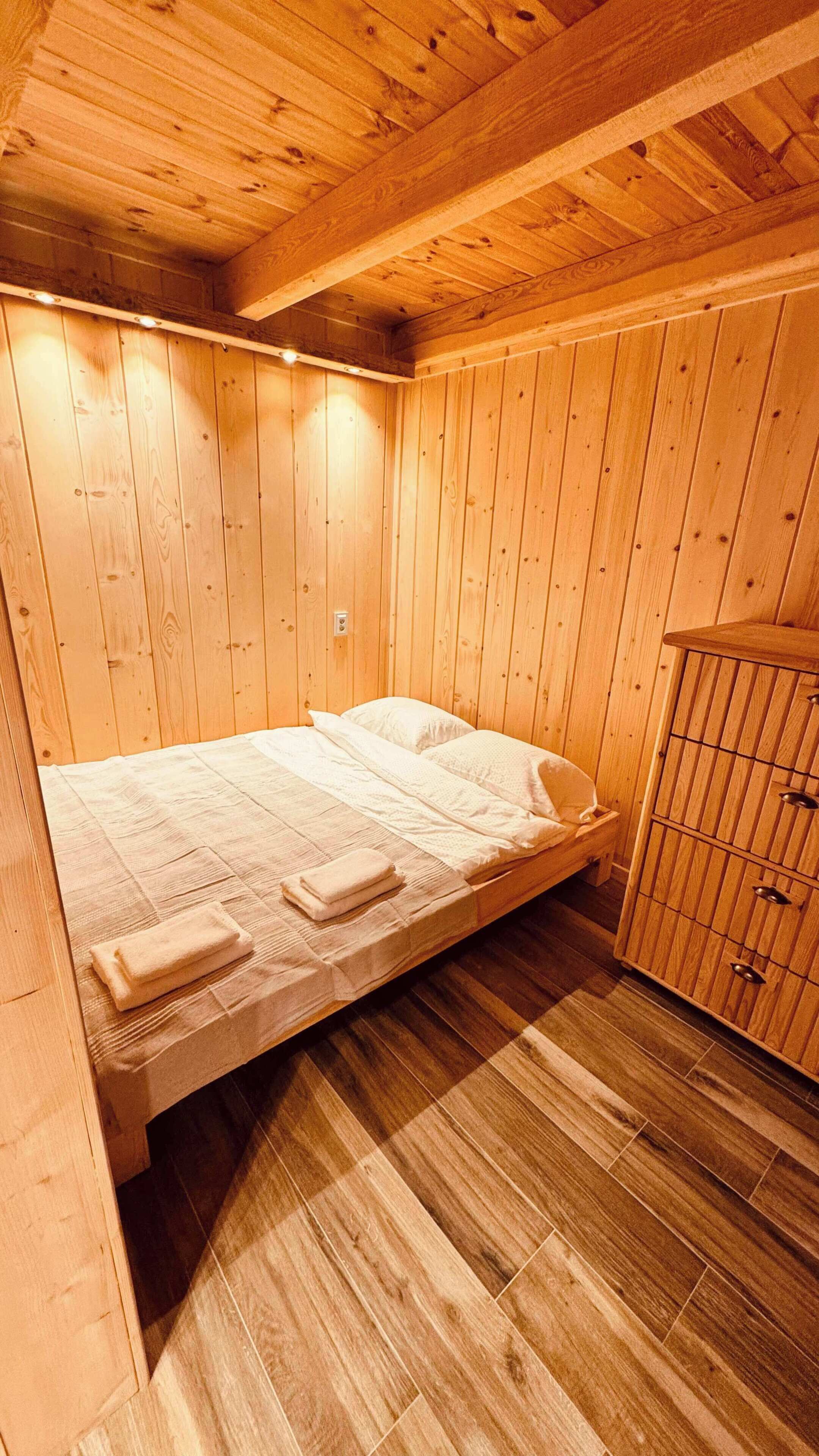 A wooden room with a bed, a cabinet, and a ceiling with exposed beams.