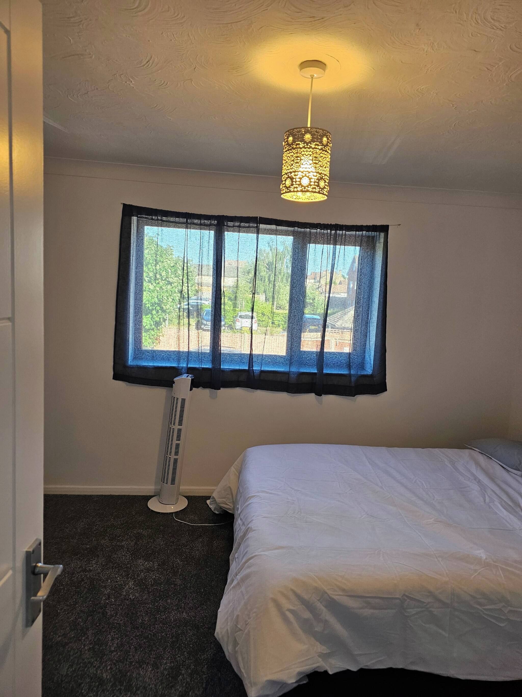Une chambre à coucher avec un lit, un radiateur mobile, une fenêtre avec des rideaux et un luminaire fixé au plafond.