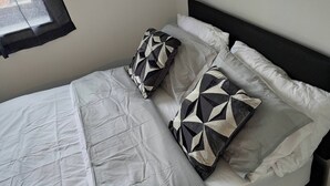Ein Bett mit weißer Daunendecke, zwei gemusterten Kissen und einem schwarzen Kopfteil.