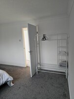 A room with a white metal shelf unit against the wall, a door leading to another room, and a grey carpeted floor.