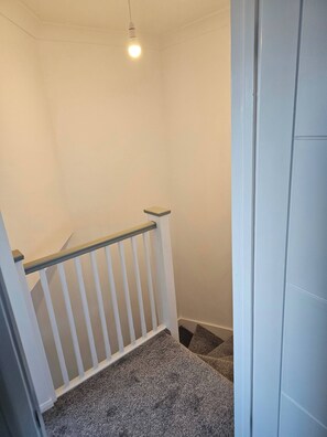 A staircase with a white railing, carpeted steps, and a light fixture. - The Chilux Stylish Apartment (Rainham)