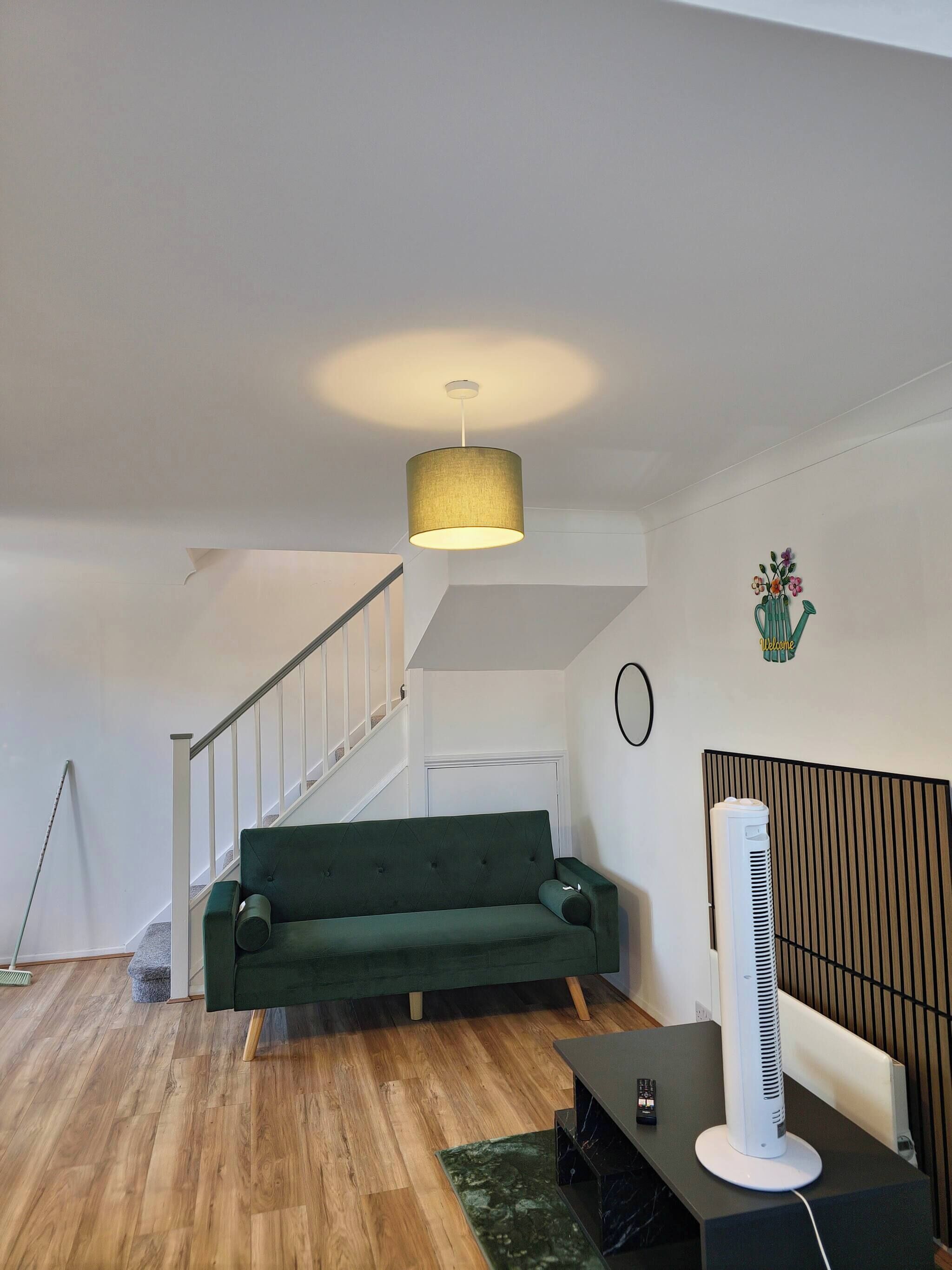 Ein modernes Wohnzimmer mit einem grünen Sofa, einem Standventilator und einer Treppe.