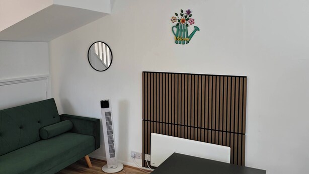 Ein modernes Wohnzimmer mit einem grünen Sofa, einem schwarzen Tisch, einem weißen Schreibtisch, einem Standheizkörper, einer Wandradiator, einer Deckenleuchte und einem Willkommensschild mit Blumen.