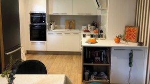 Ett modernt kök med vita skåp, en inbyggd ugn, en mikrovågsugn och en kaffebryggare.