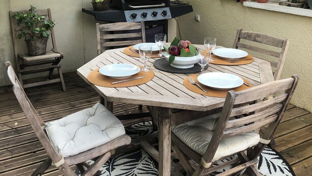 En utomhusplats för måltider med ett runt träbord, stolar och en grill.