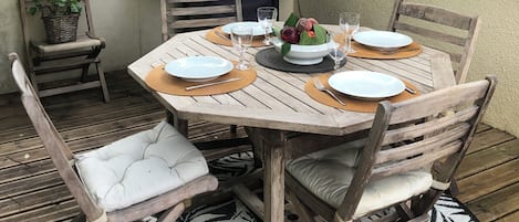 Et udendørs spiseområde med et rundt træbord, stole og en grill.