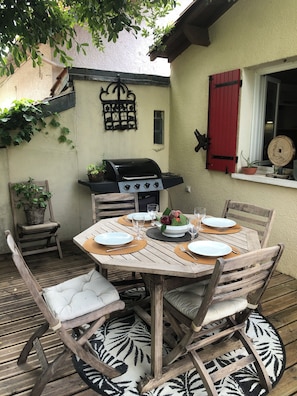 Ein Außenbereich zum Essen mit einem runden Holztisch, Stühlen und einem Grill.