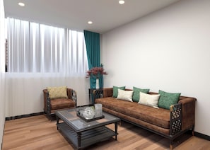 A living room with a brown sofa, two armchairs, a glass coffee table, and a vase with dried plants. - De Rond au Lac (Hanoi)