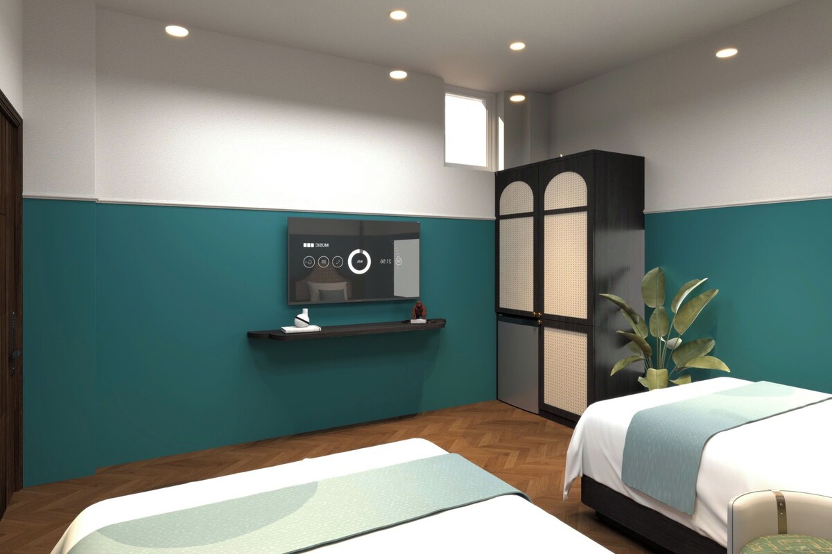 A hotel room with two beds, a TV mounted on the wall, a wardrobe, and a potted plant.