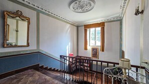A grand staircase with a wooden handrail and a metal balustrade, leading to a landing with a bookshelf and a window with curtains. - Château de Roche – French Château Living near Toulouse (Pechbonnieu)