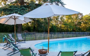 A swimming pool with lounge chairs and umbrellas, surrounded by a fence and trees. - Château de Roche – French Château Living near Toulouse (Pechbonnieu)