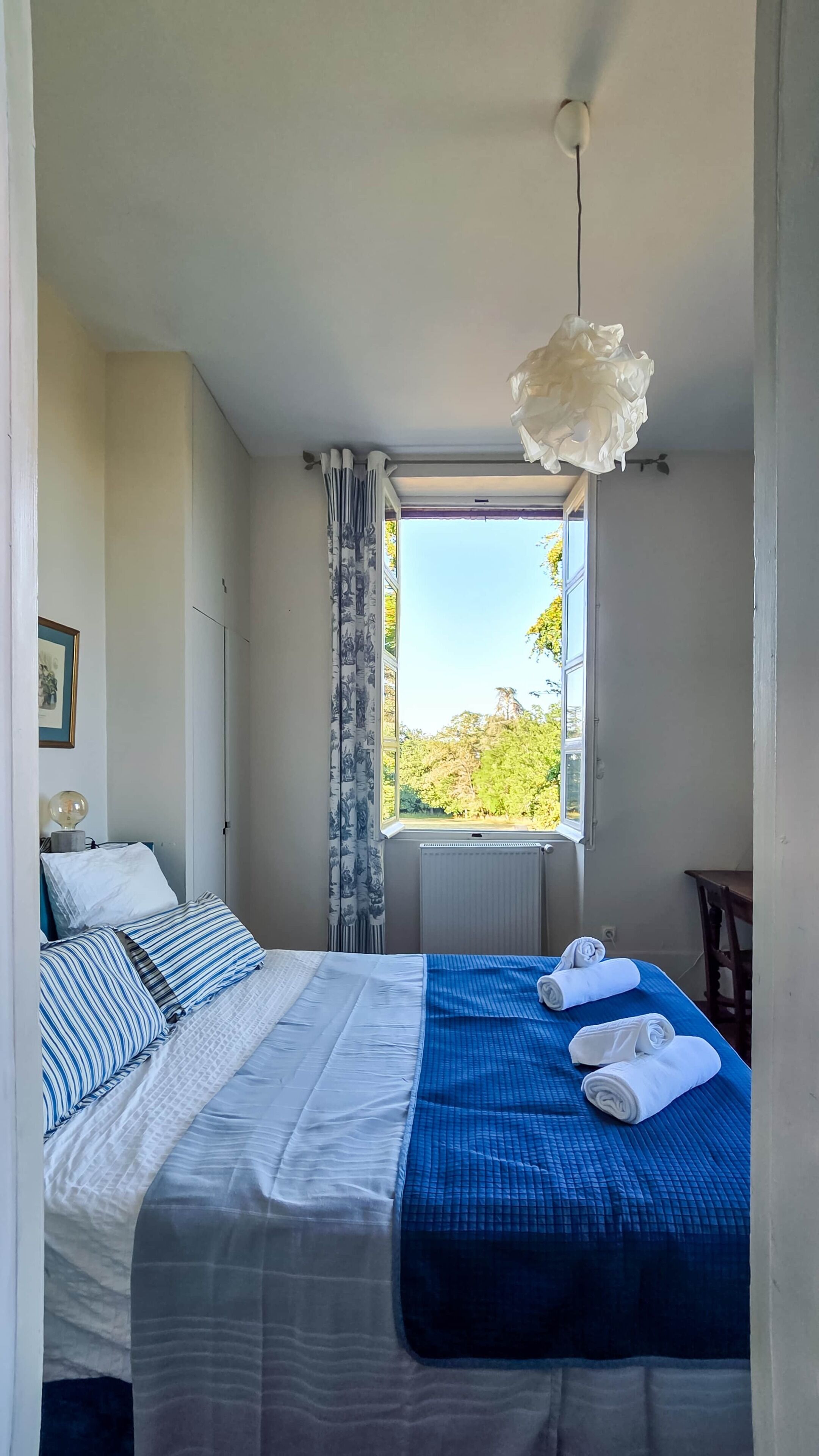 A bedroom with a bed, a window, and a hanging light fixture.