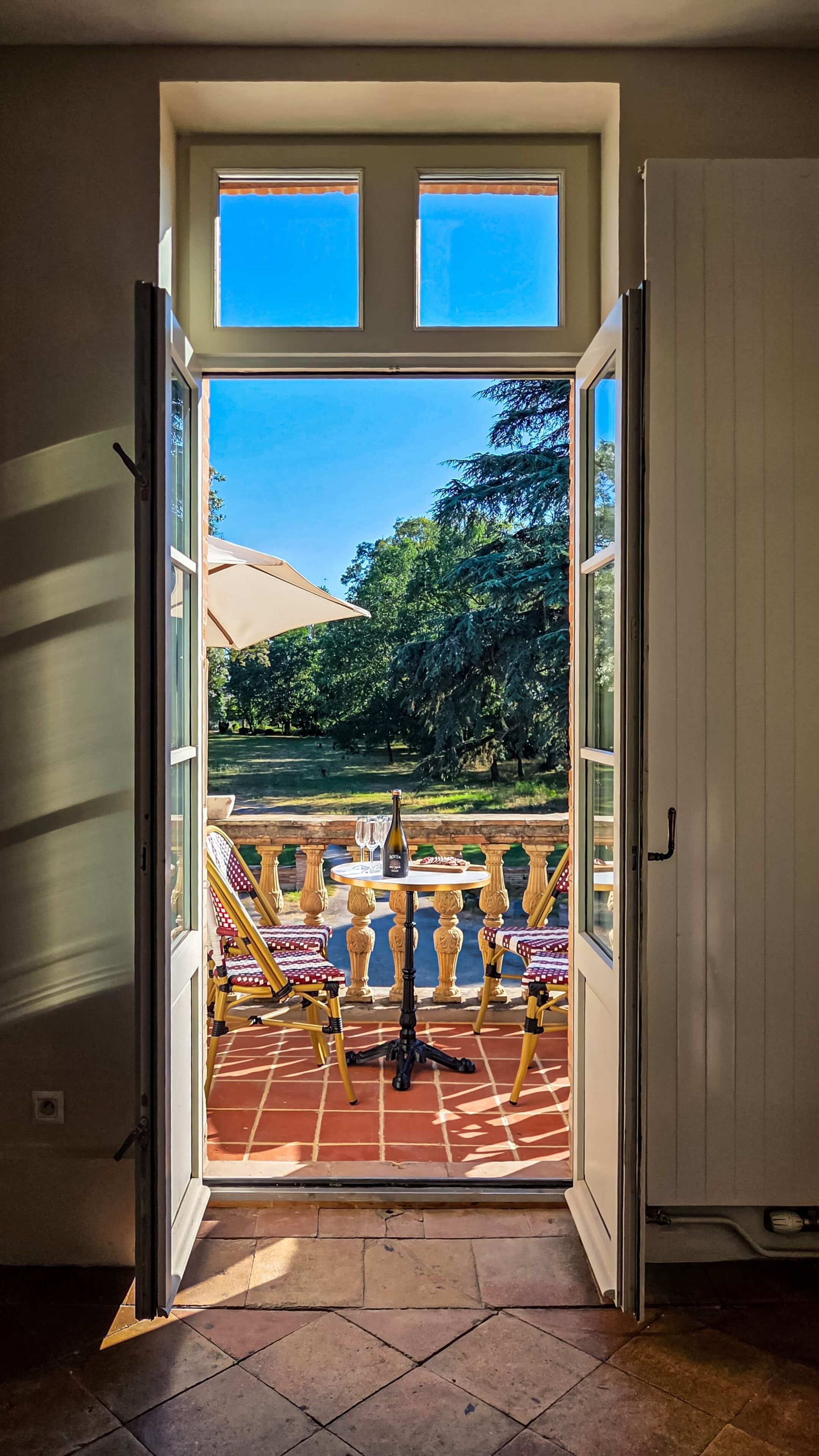 Une porte ouverte donnant sur un patio extérieur, avec une table et des chaises, une bouteille et des verres.