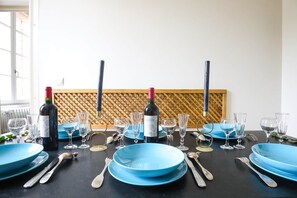 A dining table set with blue plates, wine glasses, and cutlery, with a bottle of wine and a wooden panel in the background. - Château de Roche – French Château Living near Toulouse (Pechbonnieu)