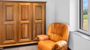 Habitación con un amplio armario de madera, un sillón de cuero y ventana con vista a la vegetación.