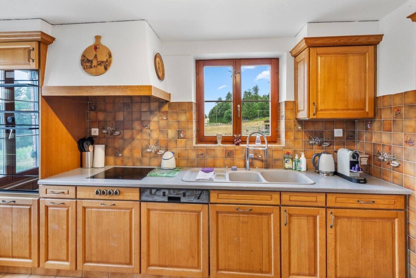 Une cuisine avec des meubles en bois, une grande fenêtre et une vue sur la verdure.