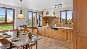 Una cocina con armarios de madera, una mesa de comedor para cuatro personas y grandes ventanas que dan a vistas de vegetación.