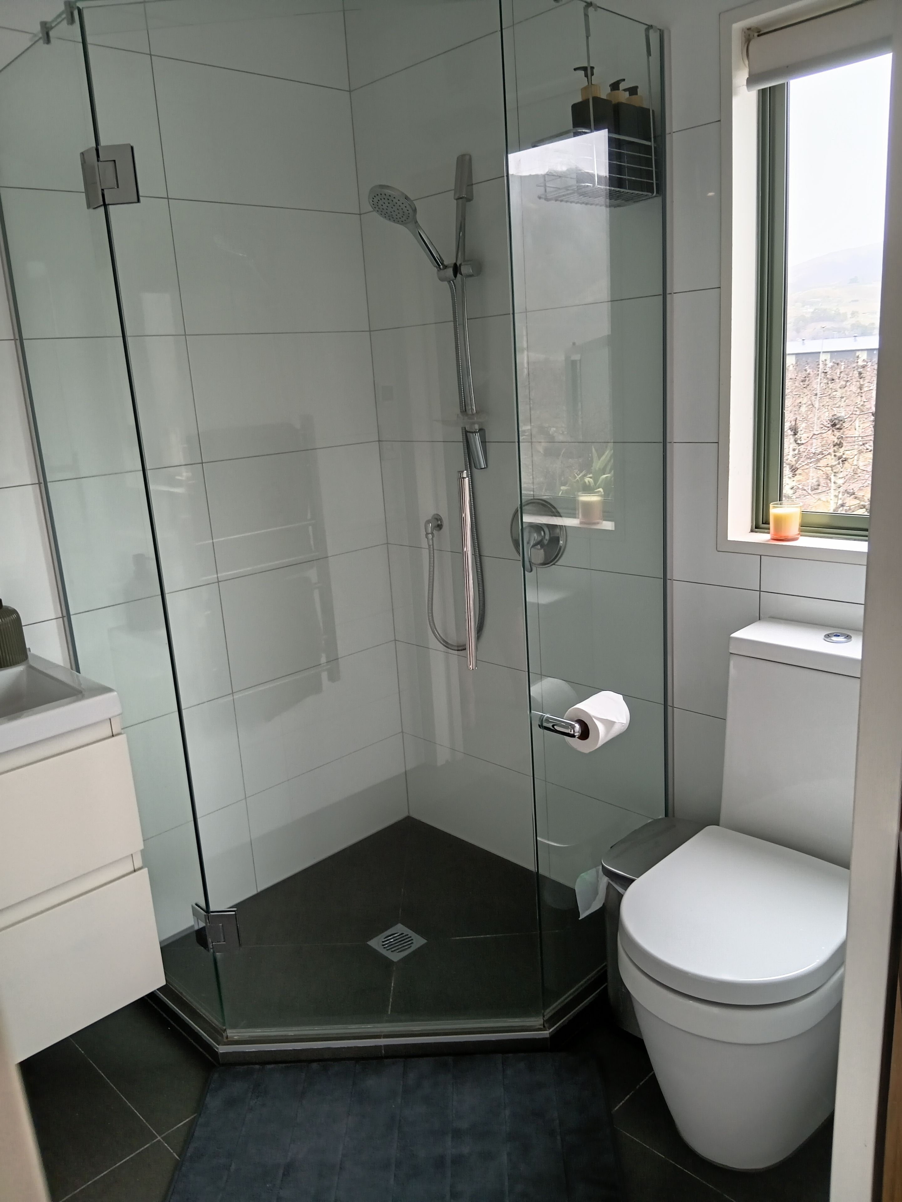 Un baño moderno con ducha de vidrio, inodoro y ventana.
