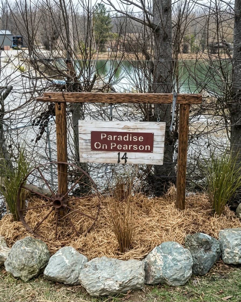 A wooden sign with the text 'Paradise on Pearson 14' in a rural setting with a body of water and trees in the background.
