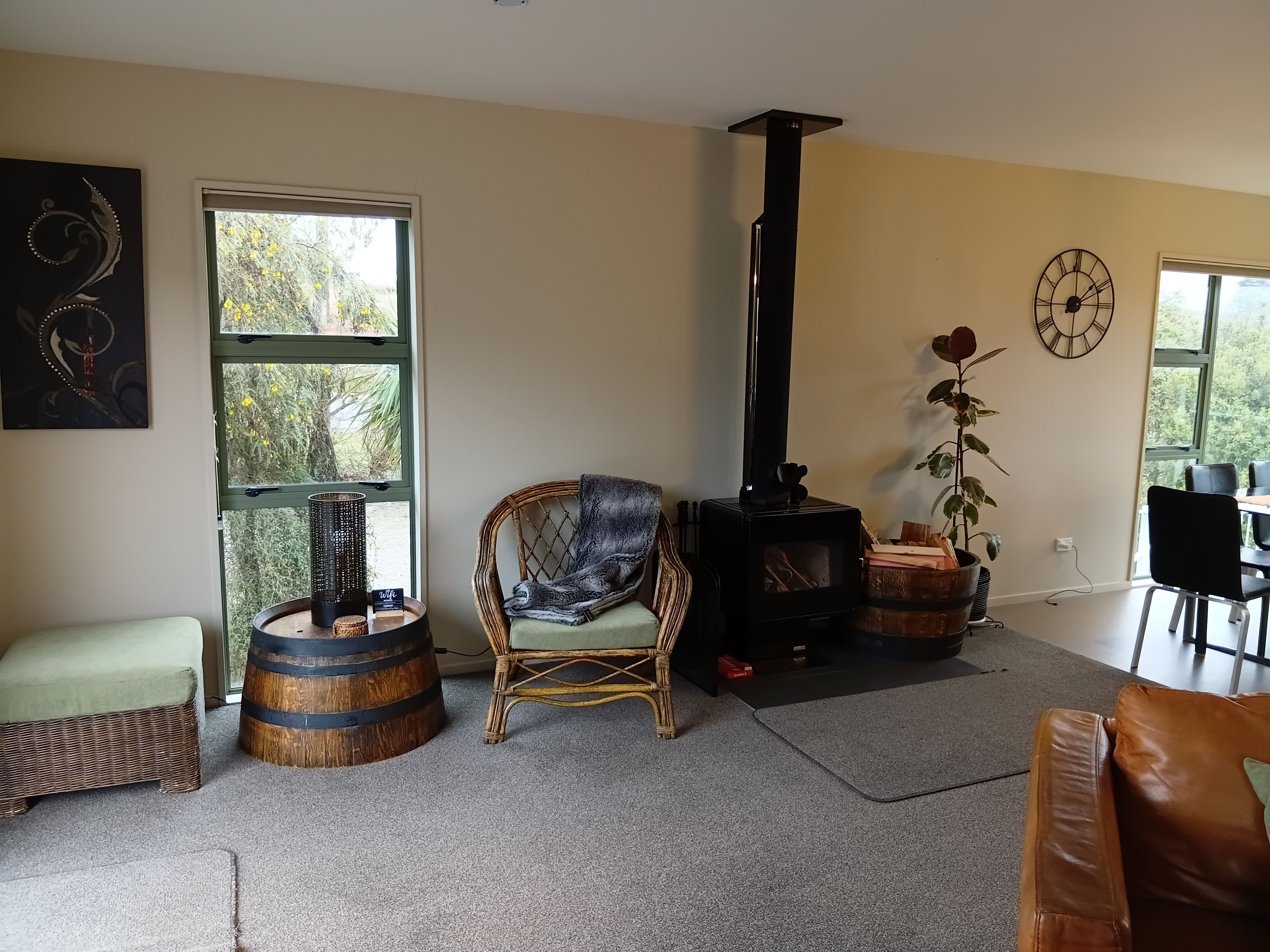 A living room with a fireplace, a green cushioned chair, a wicker sofa, and a view through a large window.