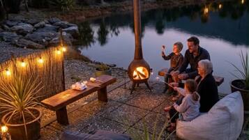 A lakeside outdoor seating area with a fire pit, benches, and potted plants.