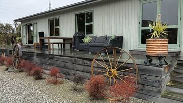 A modern house with a porch, a large wooden wheel, and a potted plant.