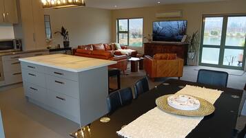 A modern kitchen with an island, a dining area with a black table, and a living room with a leather sofa and a TV.