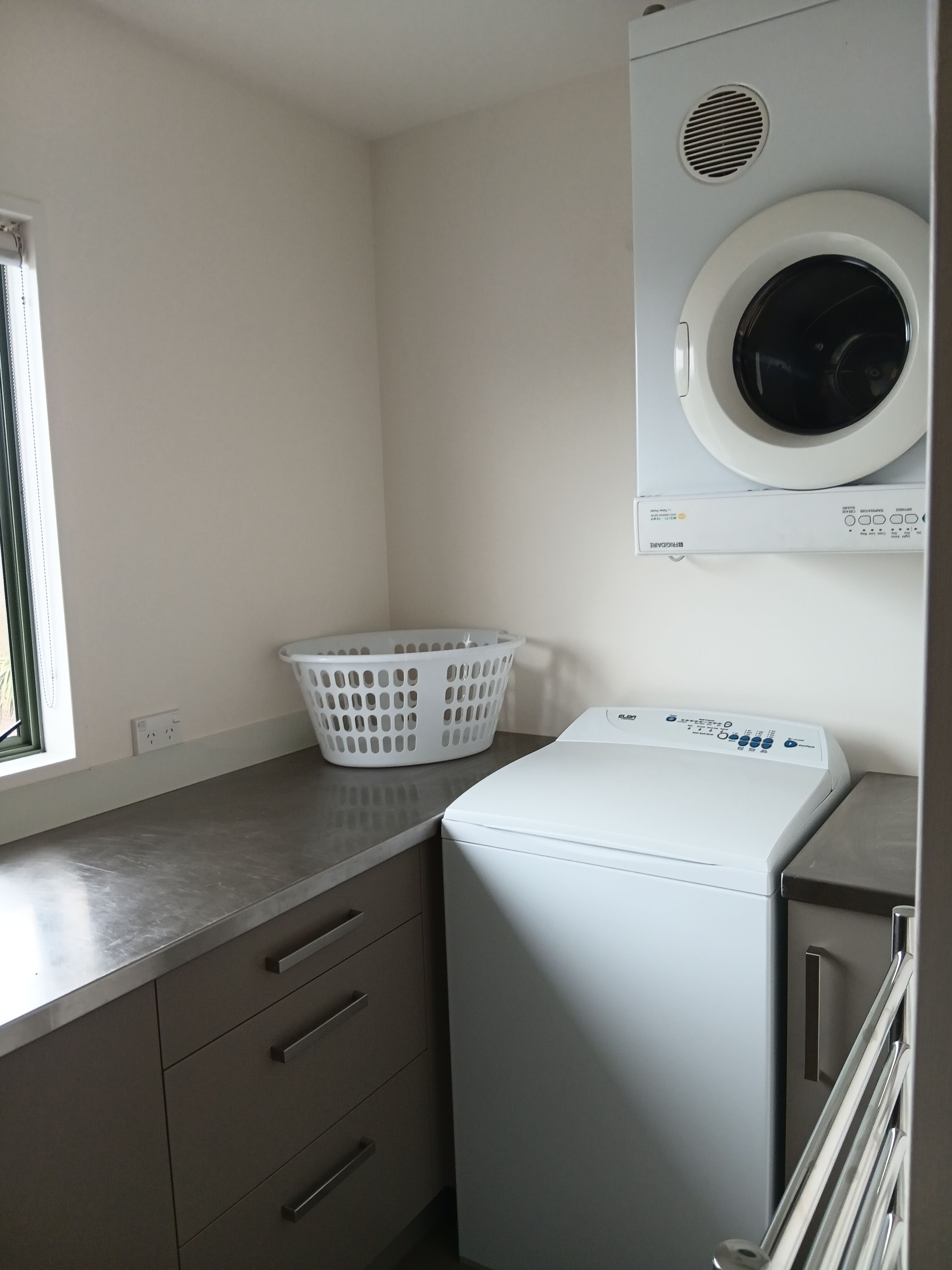 A compact laundry room with a front-loading washing machine, a white basket, and a small countertop.