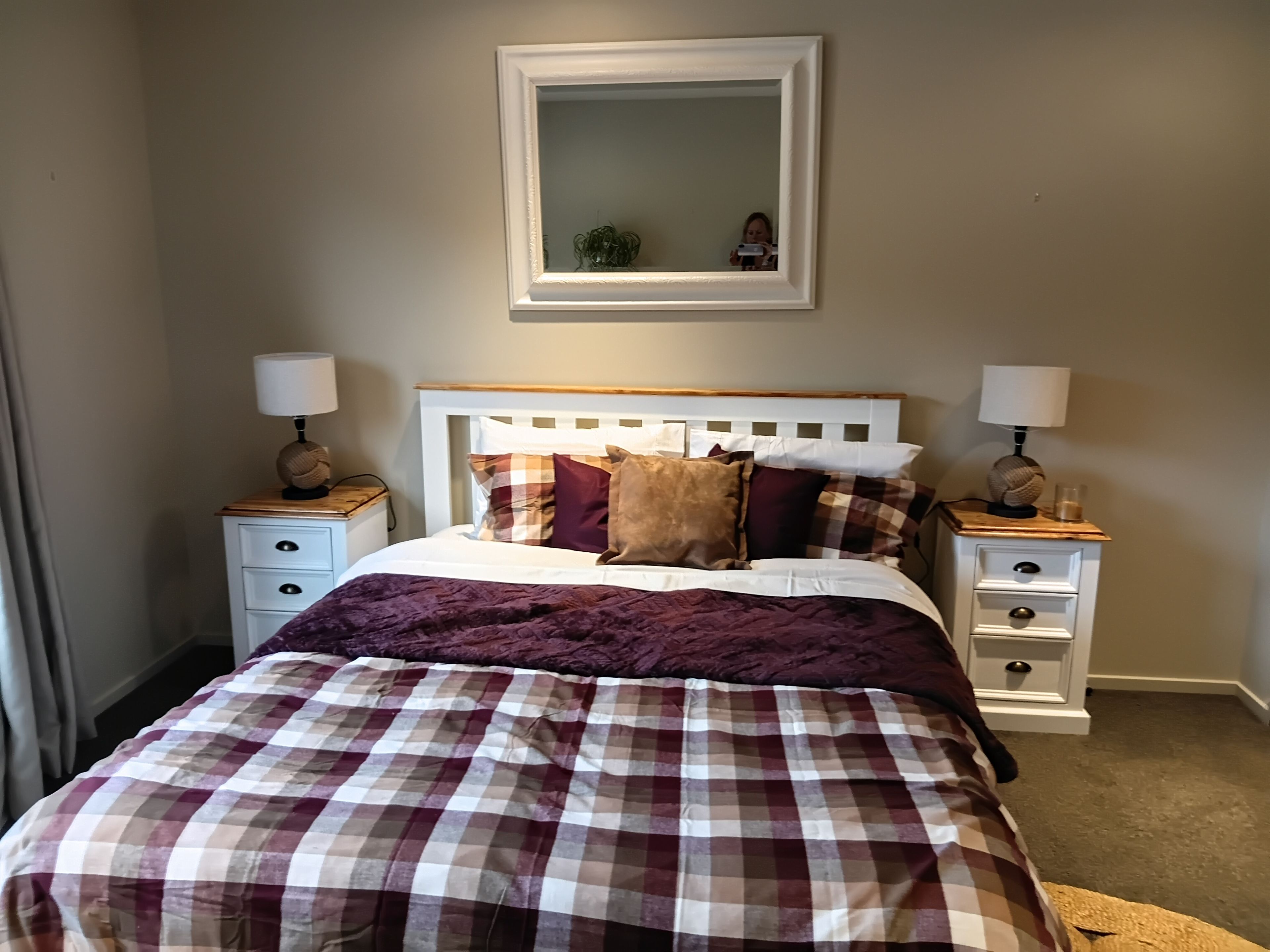 Ein Schlafzimmer mit einem Bett, zwei Nachttischen, einem Beistelltisch, einem Spiegel und einer Lampe.