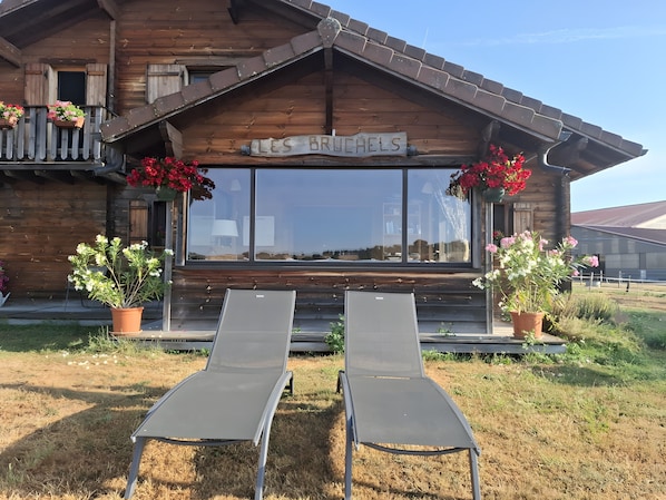 Une cabane en bois avec une pancarte indiquant « LES BRUCHELS » et deux fauteuils de jardin devant.