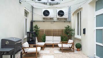 Een terras buiten met een barbecue, zithoek en airconditioners.