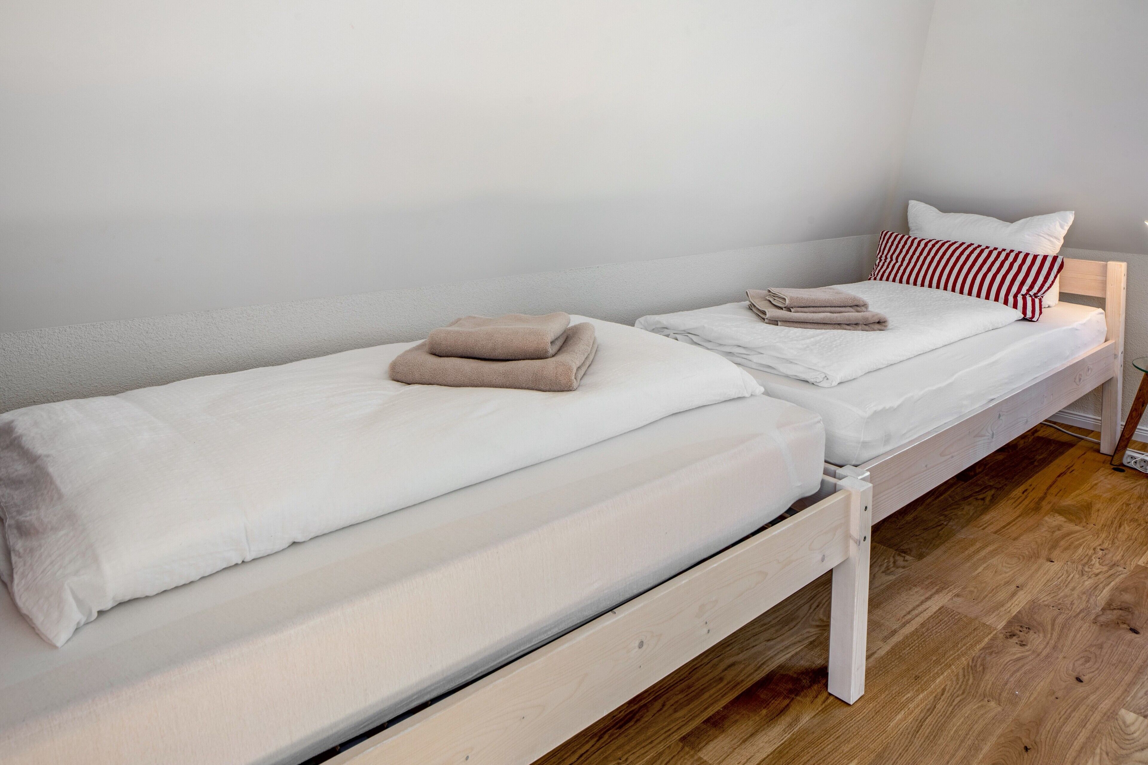 A single bed with a wooden frame, white bedding, and a red and white striped pillow.