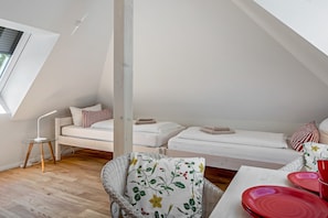 Ein modernes Schlafzimmer im Loft-Stil mit schrägem Dach, einer weißen Couch, einem Korbstuhl und einem Esstisch mit roten Tellern.