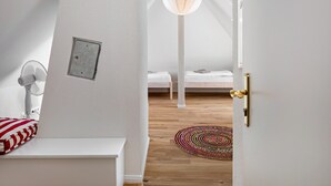 Una camera da letto con un letto bianco, un comodino, una ventola a muro e un tappeto colorato fatto a mano.