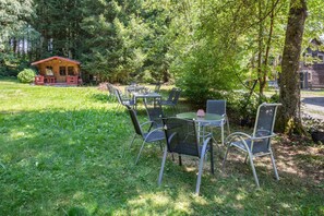 An outdoor seating area with metal chairs and tables, surrounded by lush greenery and a small wooden building in the background. - Apartment 'Fuchs und Has Feldberg - Neu Eröffnung Juli 2026 - App 7/ Gemeinschaftsgarten/ Sauna/ Aussicht' (Feldberg)